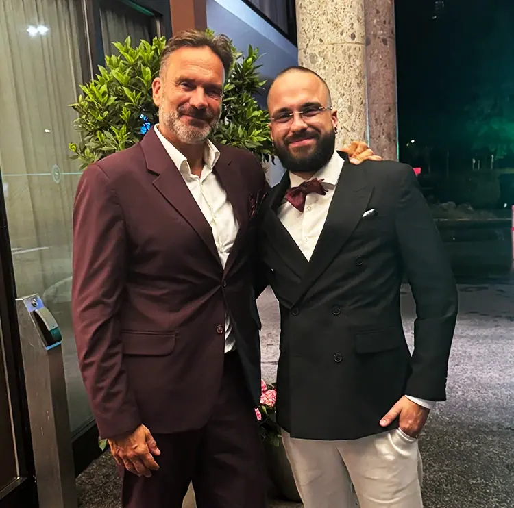 Frank Hennig und Marvin Hennig im Anzug vor einem Gebäudeeingang am Abend